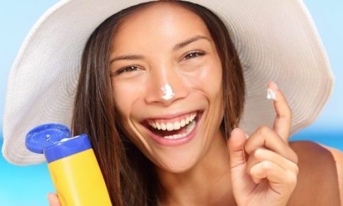 Photo of a woman at the beach applying sunscreen