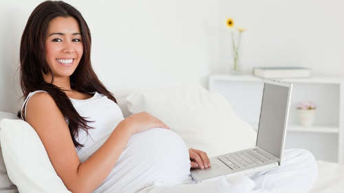 Photo of a pregnant woman at home using a laptop