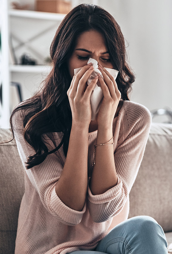 Photo of a woman sitting on the couch in her living room, blowing her nose