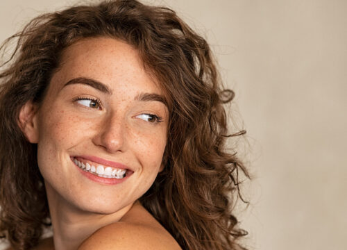 Photo of a smiling brunette woman with freckles and curly hair