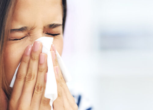 Photo of a woman blowing her nose with a tissue outside