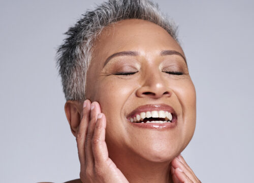 Photo of a smiling middle-age woman touching her face