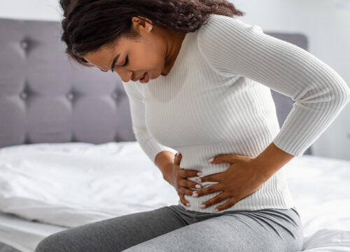 Photo of a woman clutching her abdomen while sitting on her bed